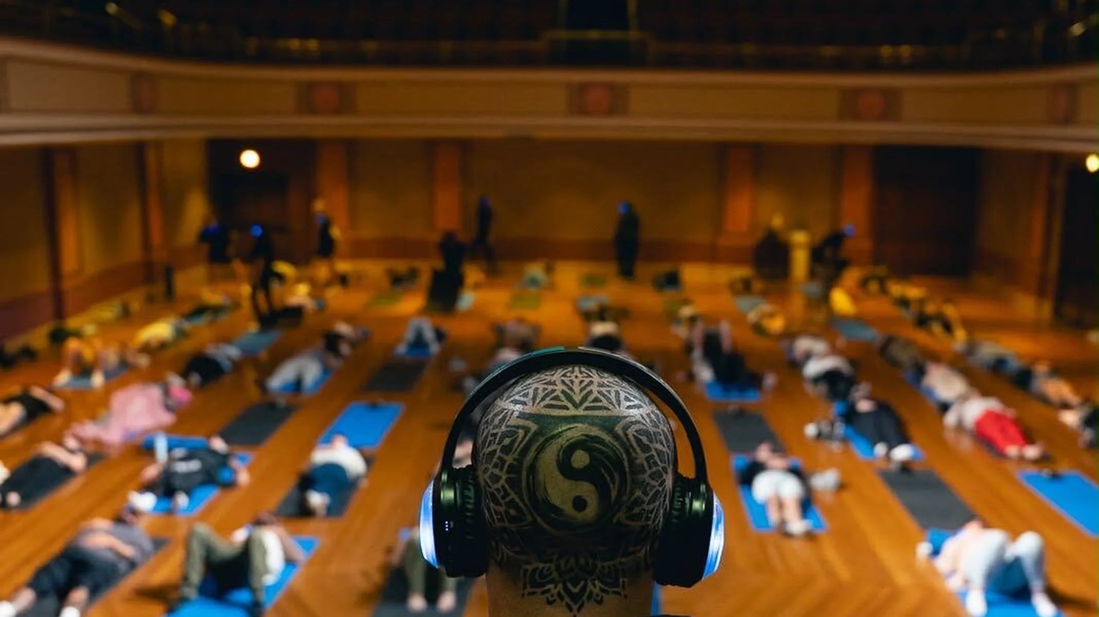 A hall of participants lying on mats during a 9D breathwork session, facilitator in the foreground